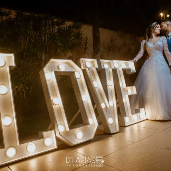 Casal ao lado do painel iluminado escrito love