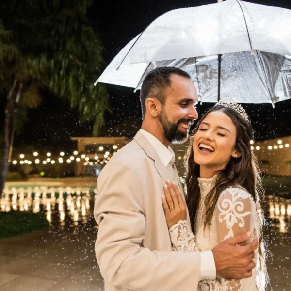 Caroline e Leonardo abraçados rindo com guarda chuva